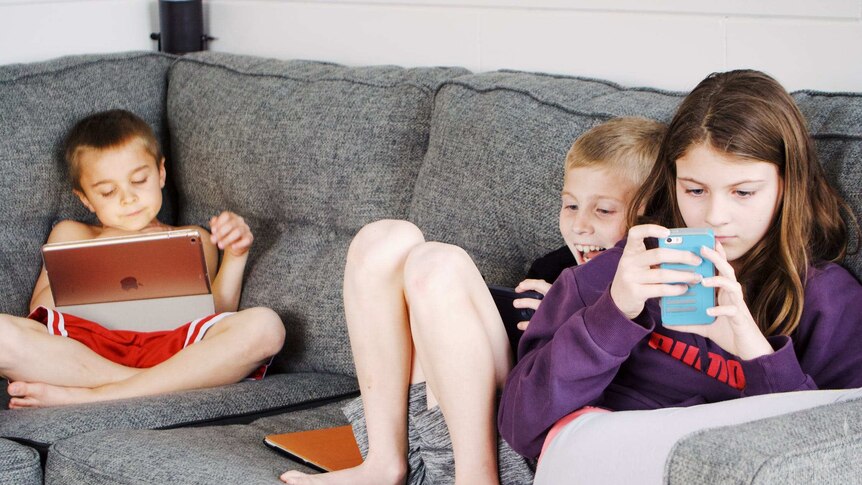 三个年轻人孩子们坐在沙发上全神贯注于手机和平板电脑。